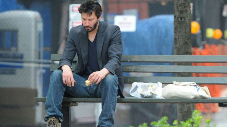 Keanu Reeves sentado en una banca comiendo helado