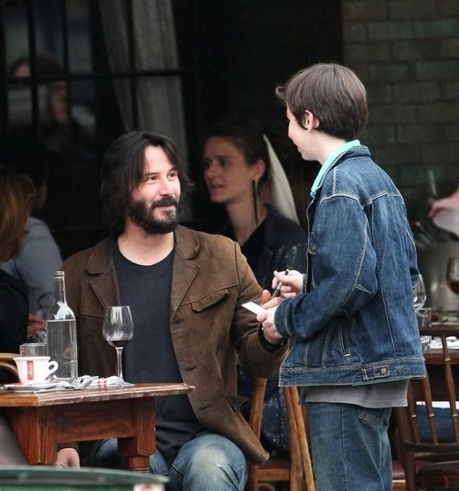 Keanu Reeves conversando con un niño mientras come