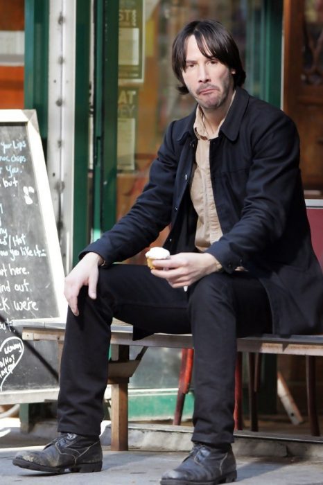 Keanu Reeves sentado en una banca comiendo un helado 