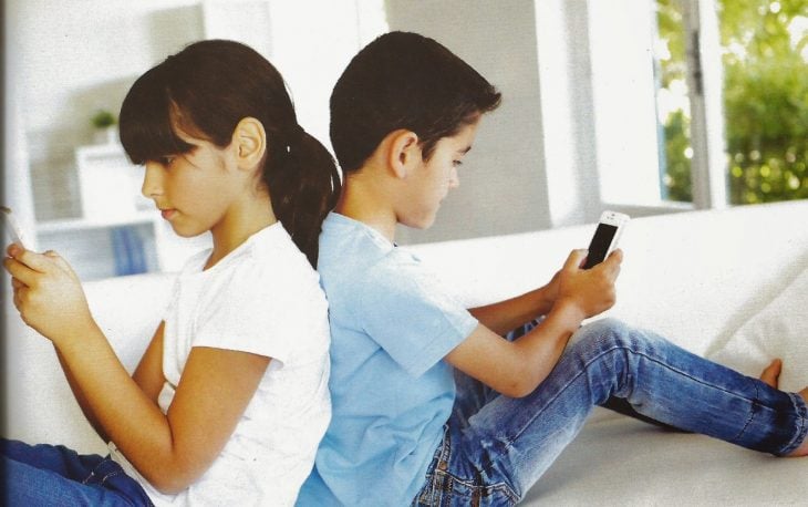 Niños sentados de espaldas revisando cada uno su celular