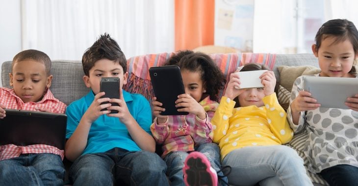 Niños sentados en unsofá sosteniendo cada uno su celular 