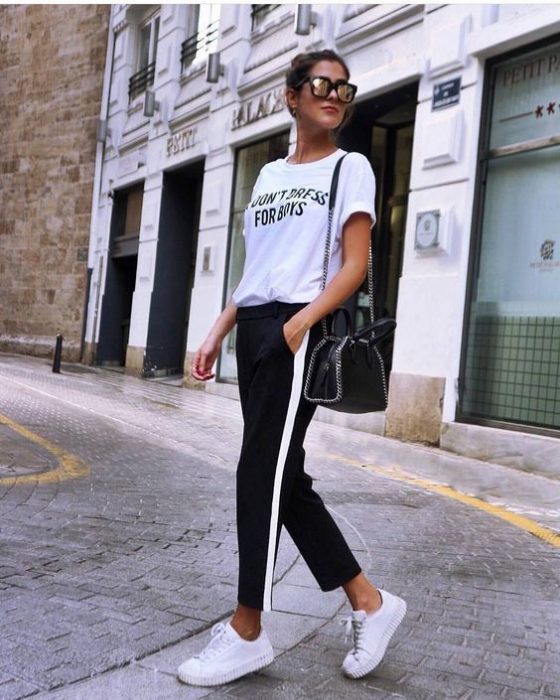 Chica usando unos tenis con pantalón negro y línea blanca y blusa de color blanco