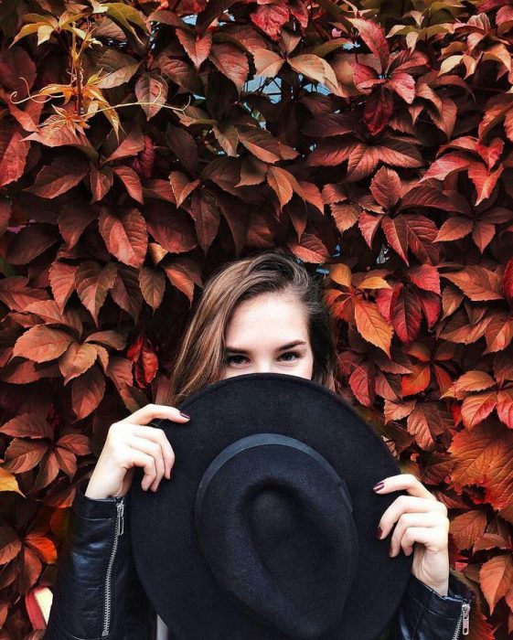 Mujer con pared de hojas naranjas y sombrero 