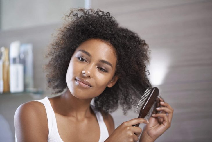 Chica de cabello chino cepillándose las puntas de la cabellera