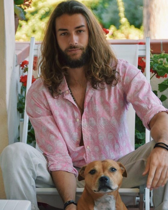 Hombre de cabello largo y barba posando junto a su perro