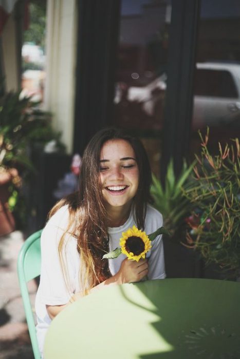 Chica riendo mientras sostiene un girasol