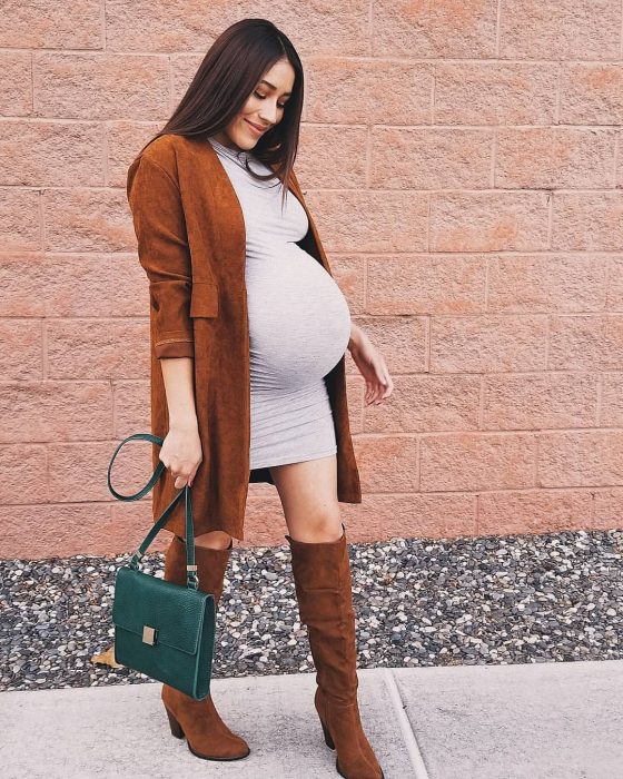 Chica embarazada usando un vestido de color gris con botas café