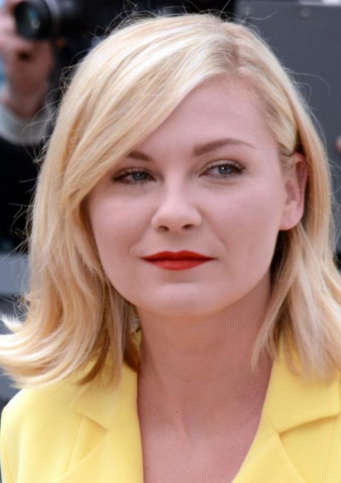 Kirsten Dunts usando una blusa amarilla y con los labios pintados de rojo 