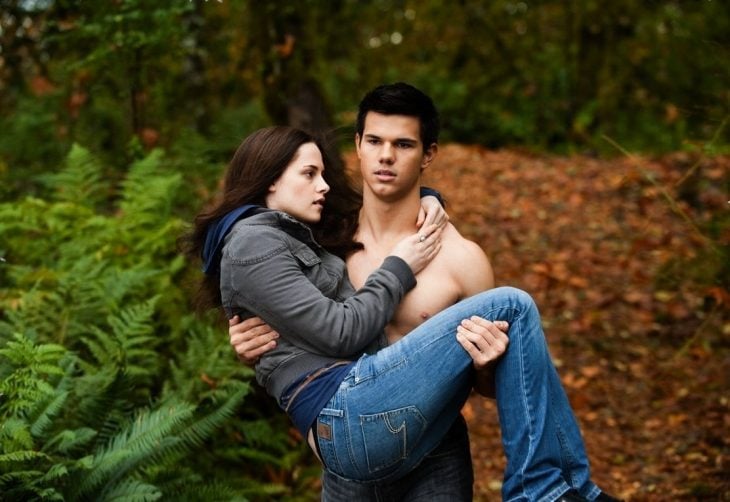 Chico musculoso carganco en brazos a una chica por el bosque
