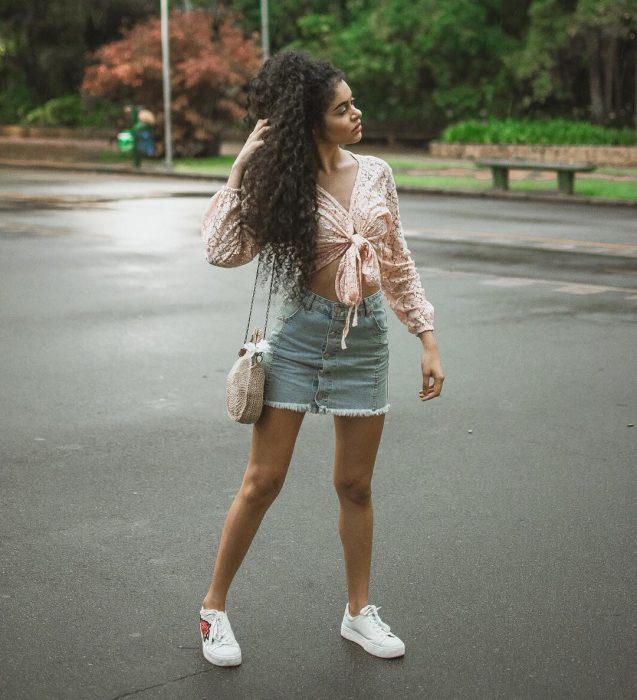 Chica de cabello chino en medio de la calle con una falda de mezclilla y tenis