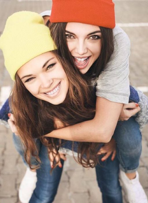 Hermana de gorro amarillo cargando a su hermana de gorro rojo