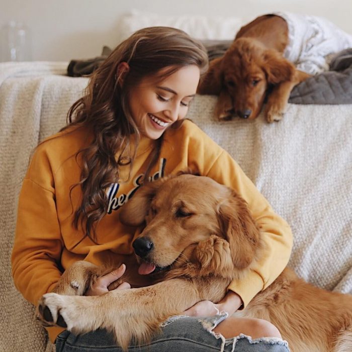 Chica con hoddie anaranjado sentada con sus dos perros golden retriever