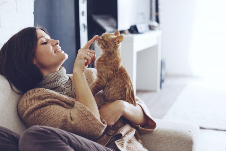 Chica de cabello corto y suéter café sonriendo y sostendiendo a un gato anaranjadi