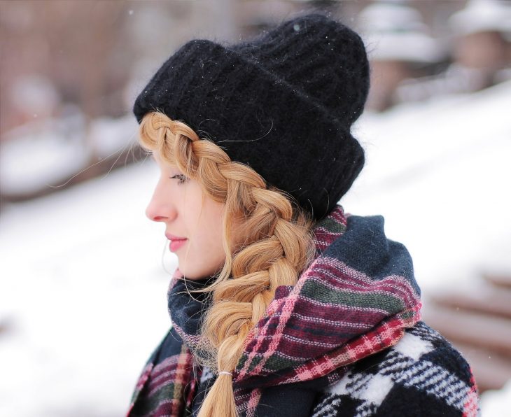 Chica de cabello rubio trenzado con gorra negra para invierno