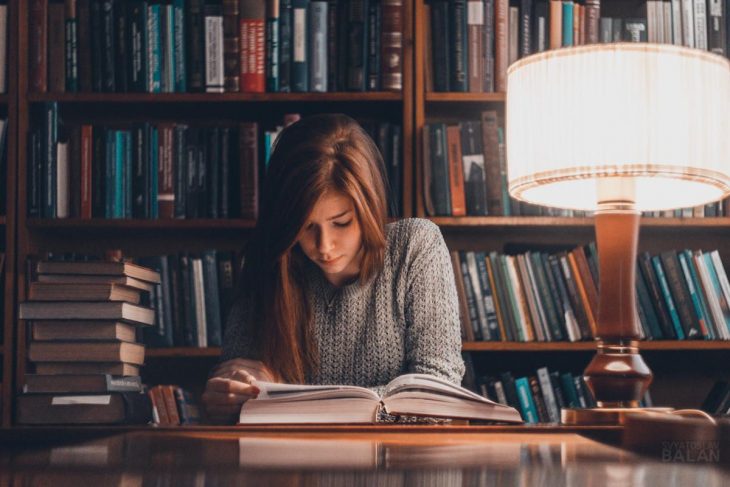 Chica joven leyendo un libro en la biblioteca