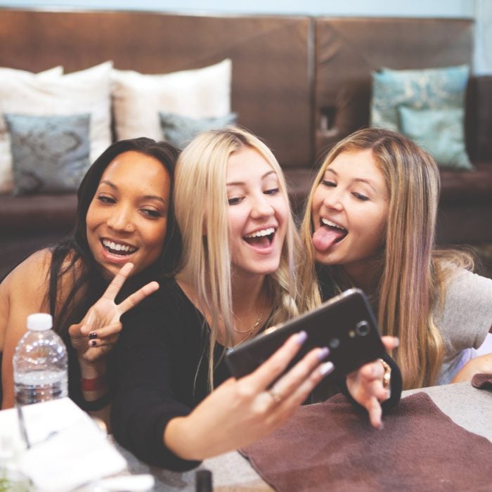 Grupo de tres amigas sonriendo mientras se toman una foto con el celular