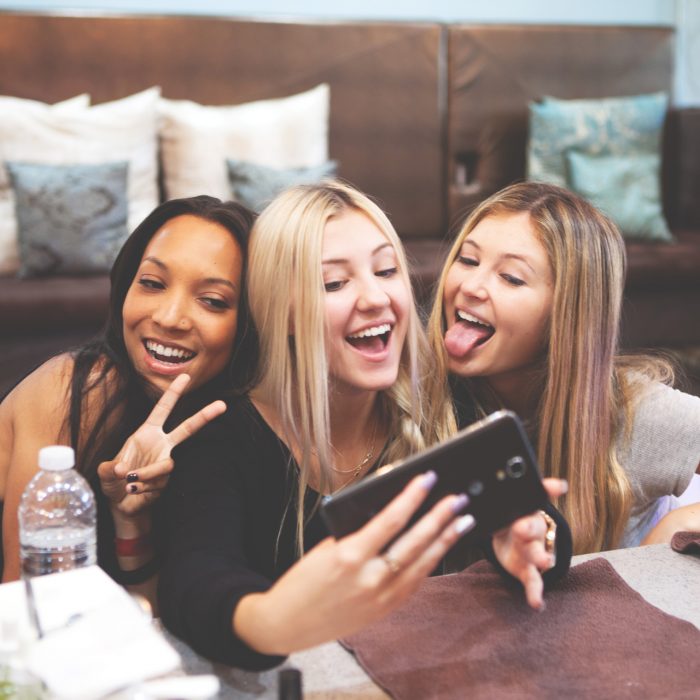 Grupo de tres amigas sonriendo mientras se toman una foto con el celular