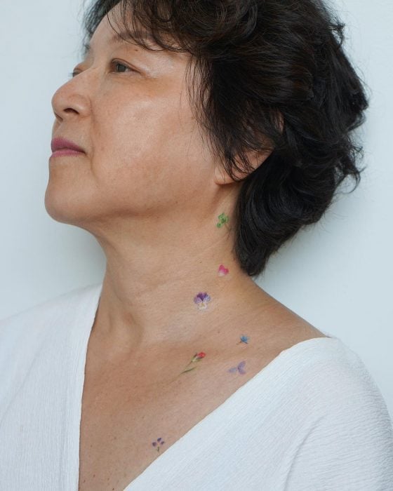 Chica con un tatuaje de un unas flores en su cuello