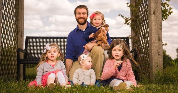 Padre con camisa azul cuidando a sus cuatro hijas sentadas en el pasto
