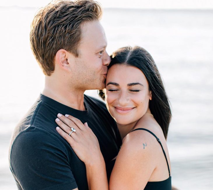 Lea Michele y Zandy Reich, pareja abrazada en la playa, mujer de cabello castaño con una blusa sin mangas y hombre pelirrojo con playera negra