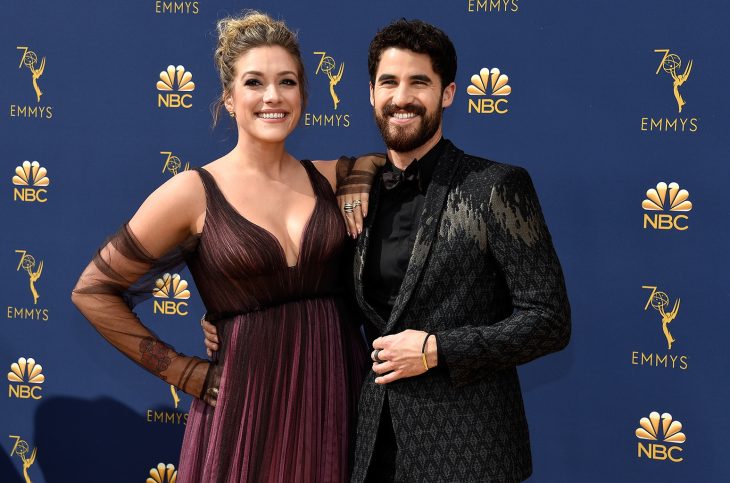 Darren Criss y Mia Swier, pareja abrazada, mujer con vestido guinda y hombre con traje negro