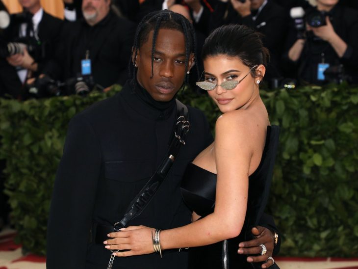 Kylie Jenner y Travis Scott, mujer con vestido negro y lentes de sol y hombre de trenzas con traje negro