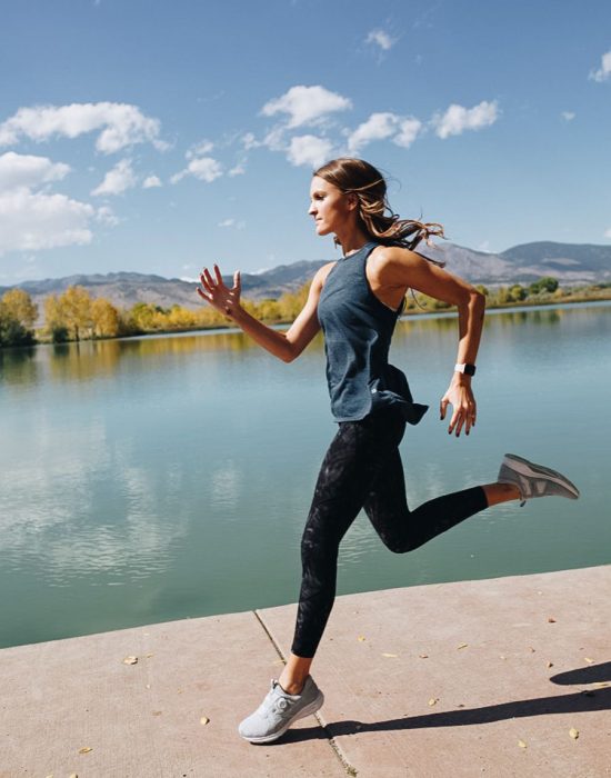 Chica de cabello largo en ropa deportiva corriendo al aire libre al lado de un lago