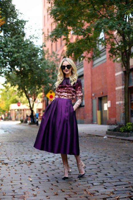 Chica rubia en calle empedrada usando blusa morada de animal print y falda midi de satín color morado