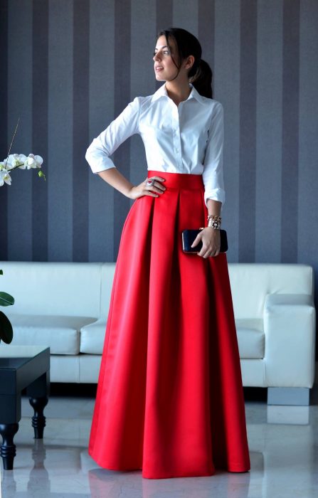 Chica de cabello castaño con una coleta vestida con una falda larga de satín roja y una blusa blanca formal