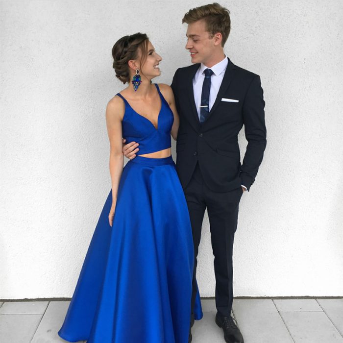 Pareja de novios posando para una foto de graduación vestidos con traje negro y top y falda de satín azul