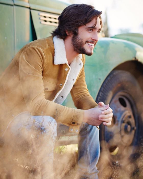 Diego Boneta, chico con chamarra color camello sentado en un carro y sonriendo