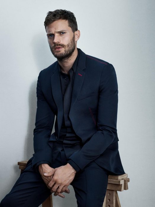 Jamie Dornan, hombre de cabello corto y traje azul sentado en un banco