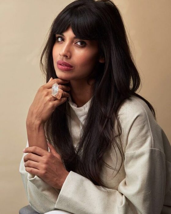 Mujer morena de cabello castaño, lacio y largo con un hoddie blanco y un anillo de piedra