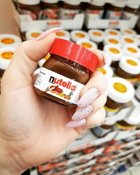 Chica con uñas largas y rosas sosteniendo una mini botella de nutella