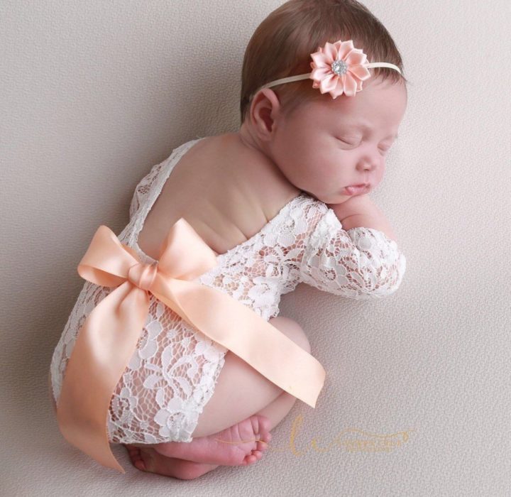 Bebé niña recostada sobre un puff durante una sesión de fotos usando un pañalero de encaje en color blanco con un moño durado