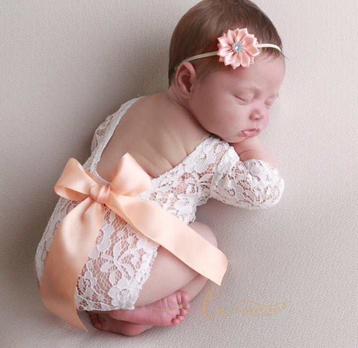 Bebé niña recostada sobre un puff durante una sesión de fotos usando un pañalero de encaje en color blanco con un moño durado 