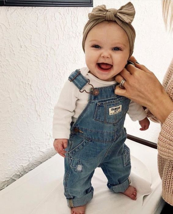 Bebé niña sonriendo mientras su mamá le coloca la ropa