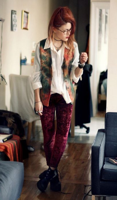 Chica pelirroja con estilo bohemio, usando una camisa blanca y chaleco con pantalones de terciopelo rojo y botines