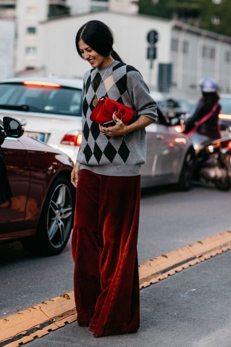 Chica de cabello agarrado en coleta con suéter amplio de rombos y pantalón holgado de terciopelo rojo