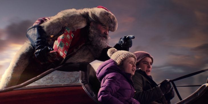 Santa Claus volando en el trineo con dos niños con chamarras