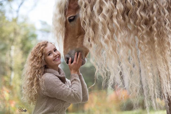 mujer rubia con cabello rizado arriba de un caballo 