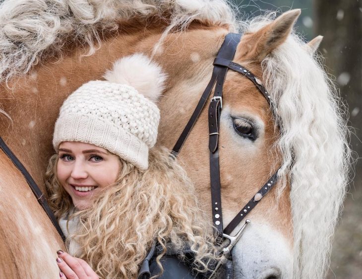 mujer rubia con cabello rizado arriba de un caballo 