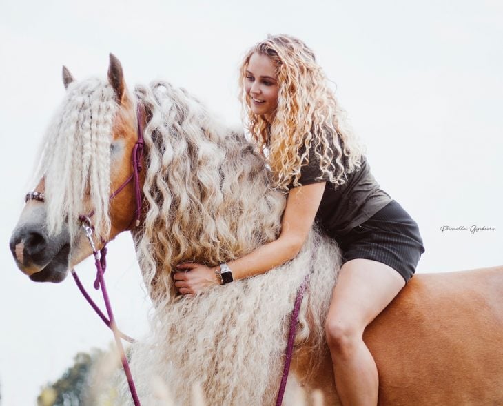 mujer rubia con cabello rizado arriba de un caballo 