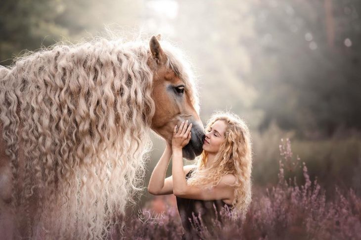 mujer rubia con cabello rizado arriba de un caballo 