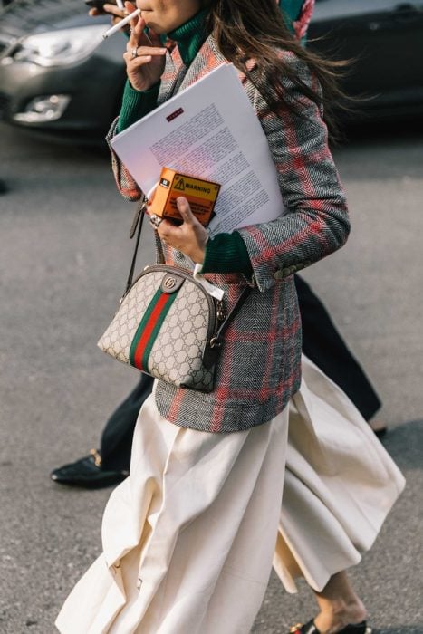 mujer con saco de cuadros y bolso y logo enfrente 