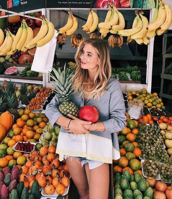 Chica sosteniendo una piña y un mango en un mercado 