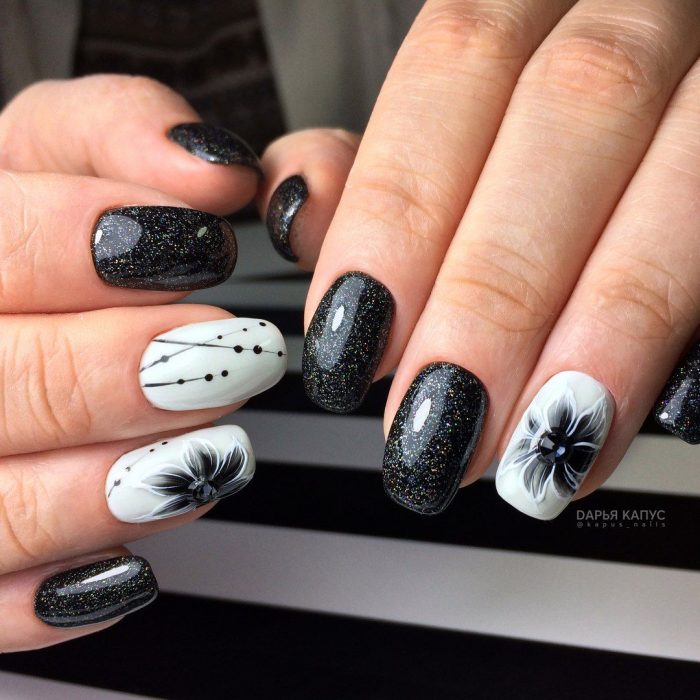 Uñas pintadas de negro y blanco con diseño de flores y puntos