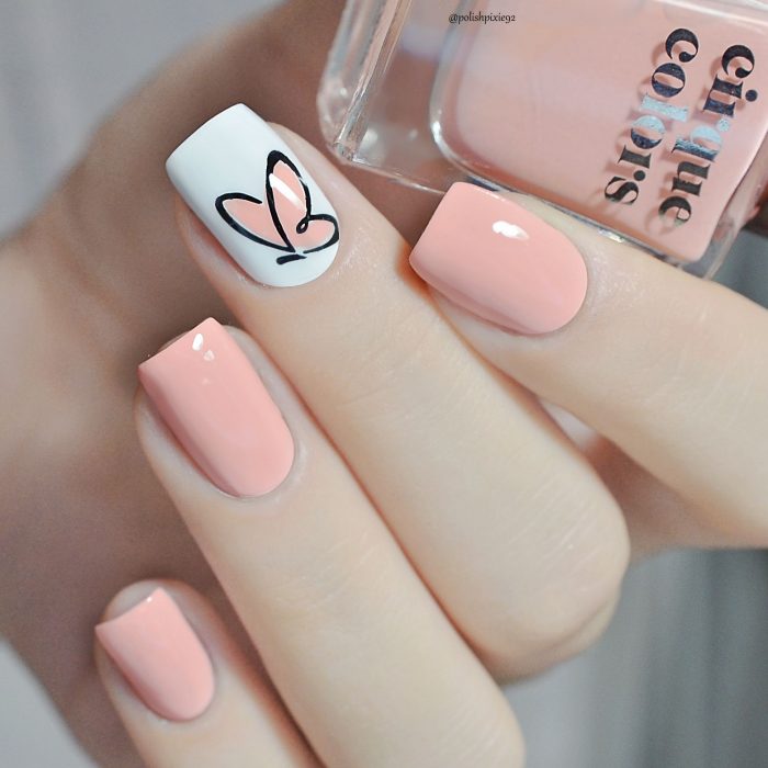 Uñas pintadas con esmalte color coral y blanco con diseño de mariposa minimalista