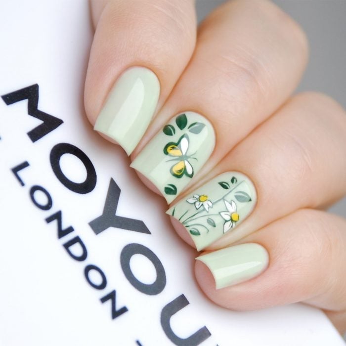 Uñas pintadas con esmalte verde con diseño de flores y mariposas