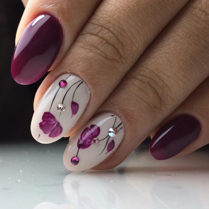 Uñas pintadas con esmalte morado y blanco con diseño de flores y puntos